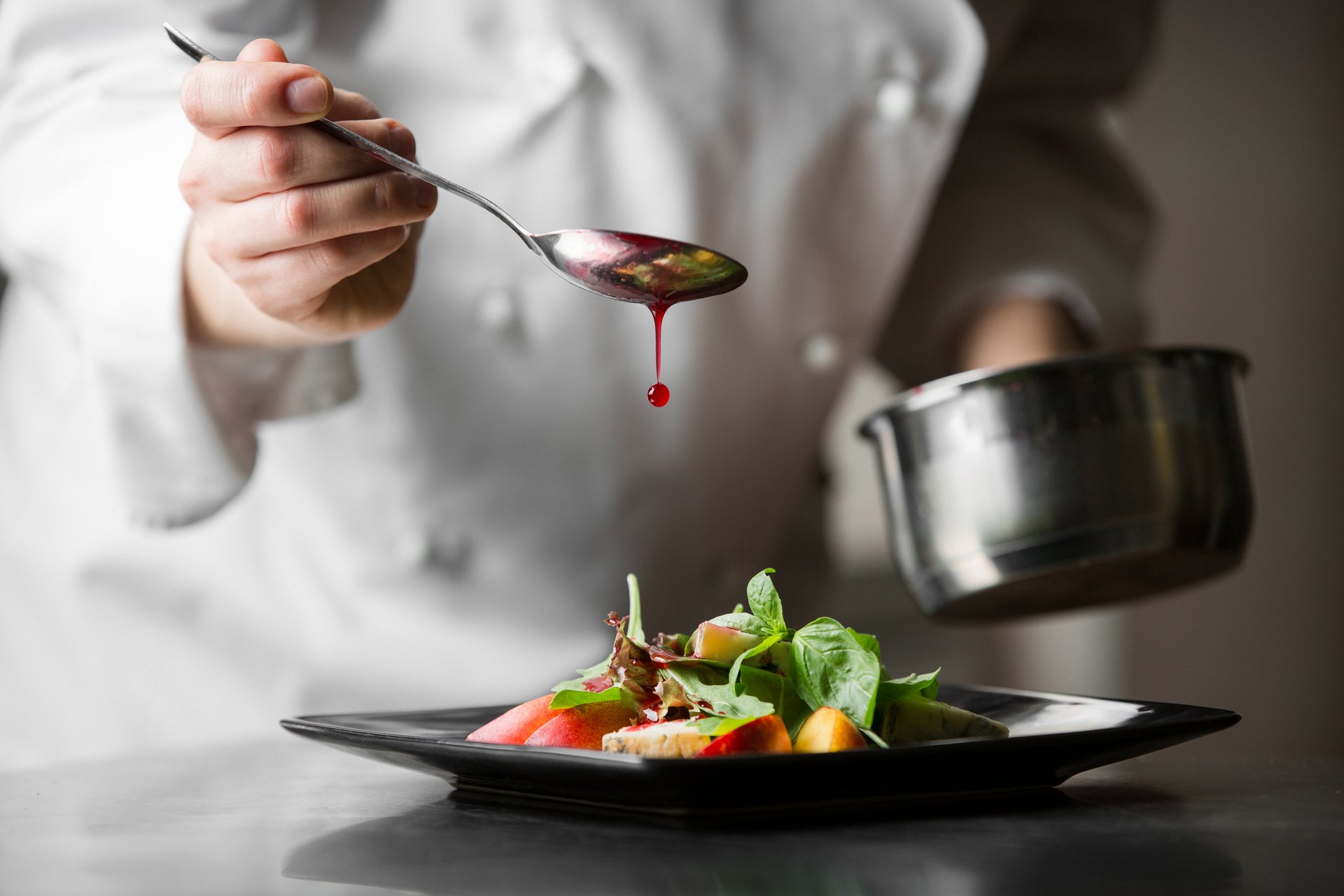 Close-up of a chef spooning dressing over a dish of fresh salad