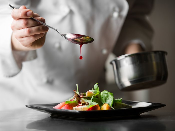 Close-up of a chef spooning dressing over a dish of fresh salad