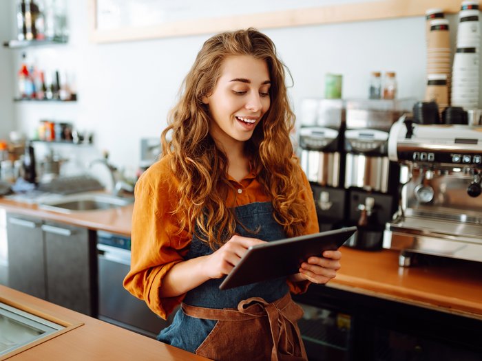 Bistro employee standing by coffee machine using digital procurement technology on a tablet