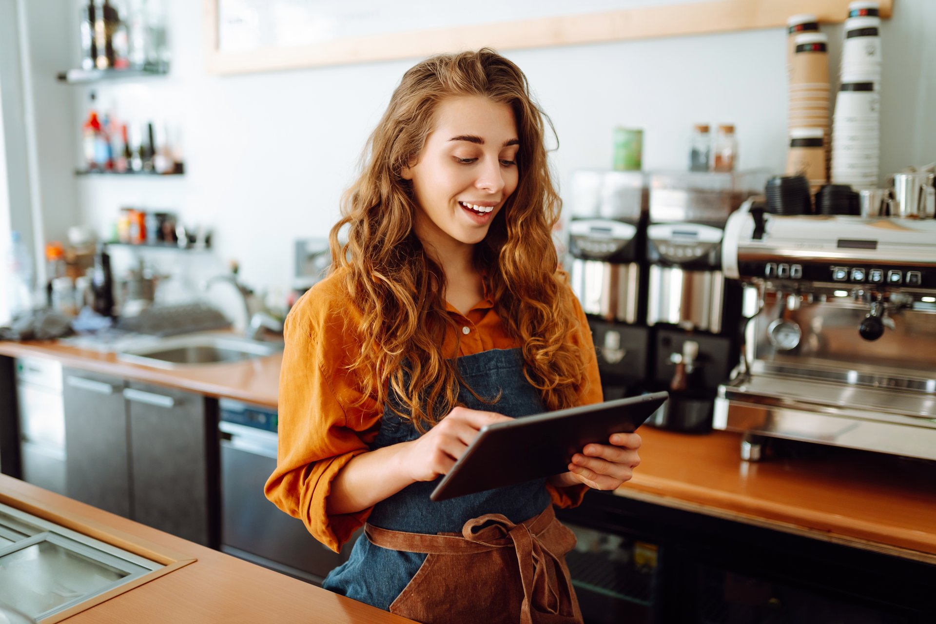 Bistro employee standing by coffee machine using digital procurement technology on a tablet