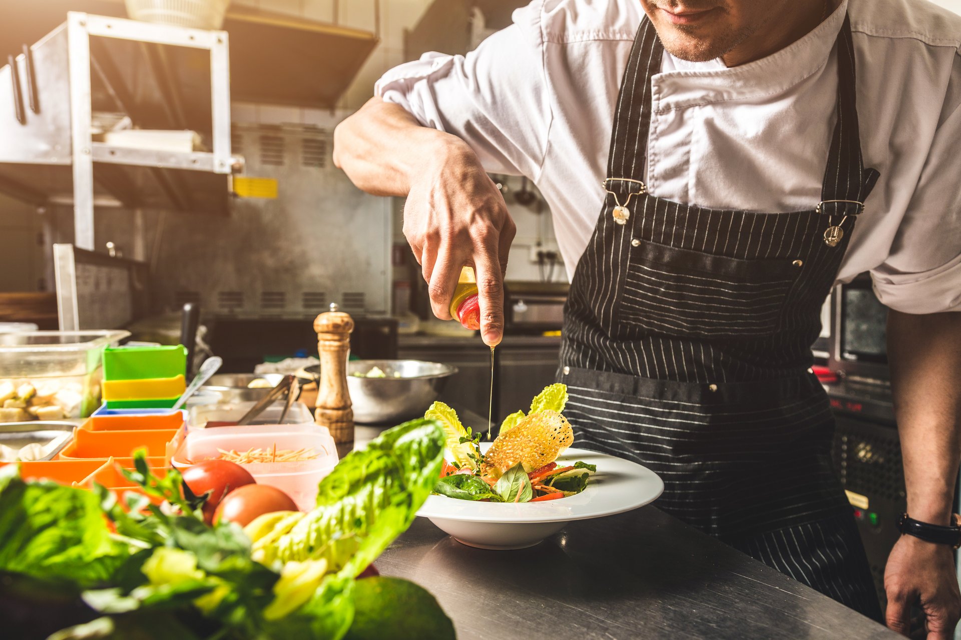 Chef in restaurant kitchen adding seasoning to a dish of freshly prepared food