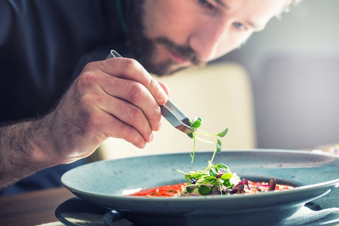 Close-up of a chef adding garnish to a dish of food.