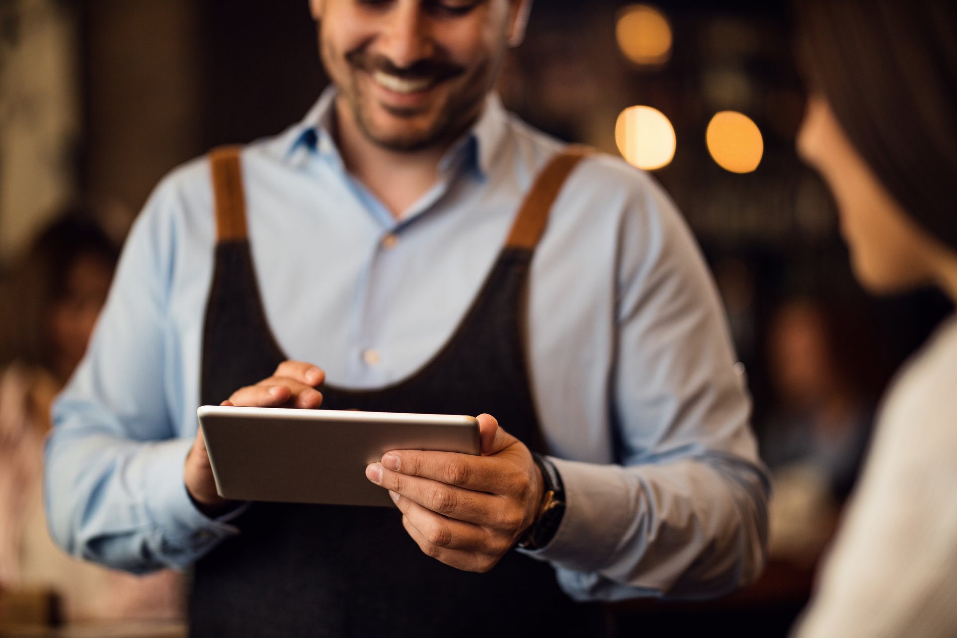 Smiling restaurant employee using tablet while talking to customer